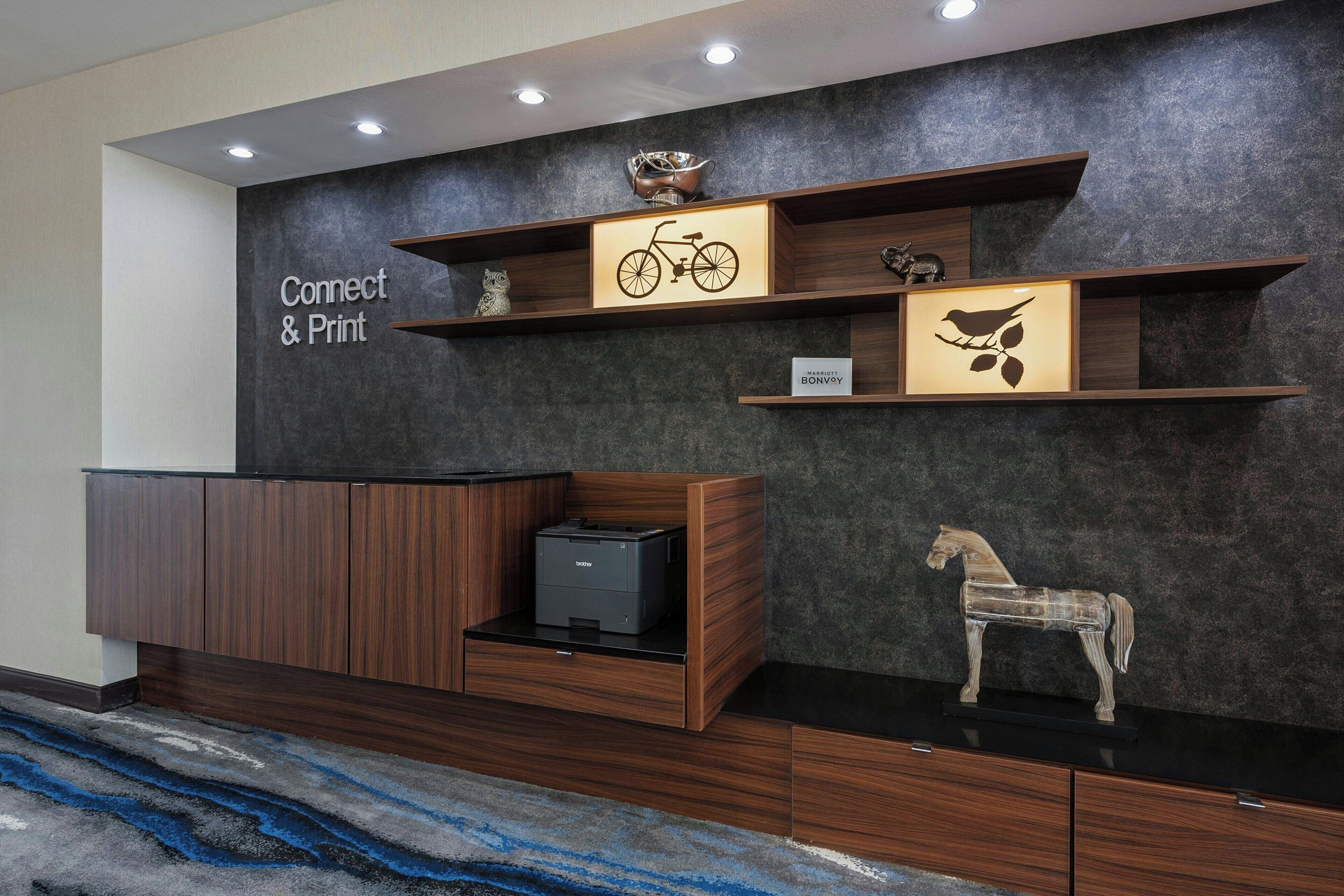 A reception area with a dark textured wall, wooden shelving with decorative items, a sign reading 'Connect & Print,' and a printer on a counter.