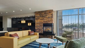 A modern living room with a stone fireplace, yellow sofa, green armchairs, and a large window with a view. - Fairfield Inn & Suites Alamosa (Alamosa)