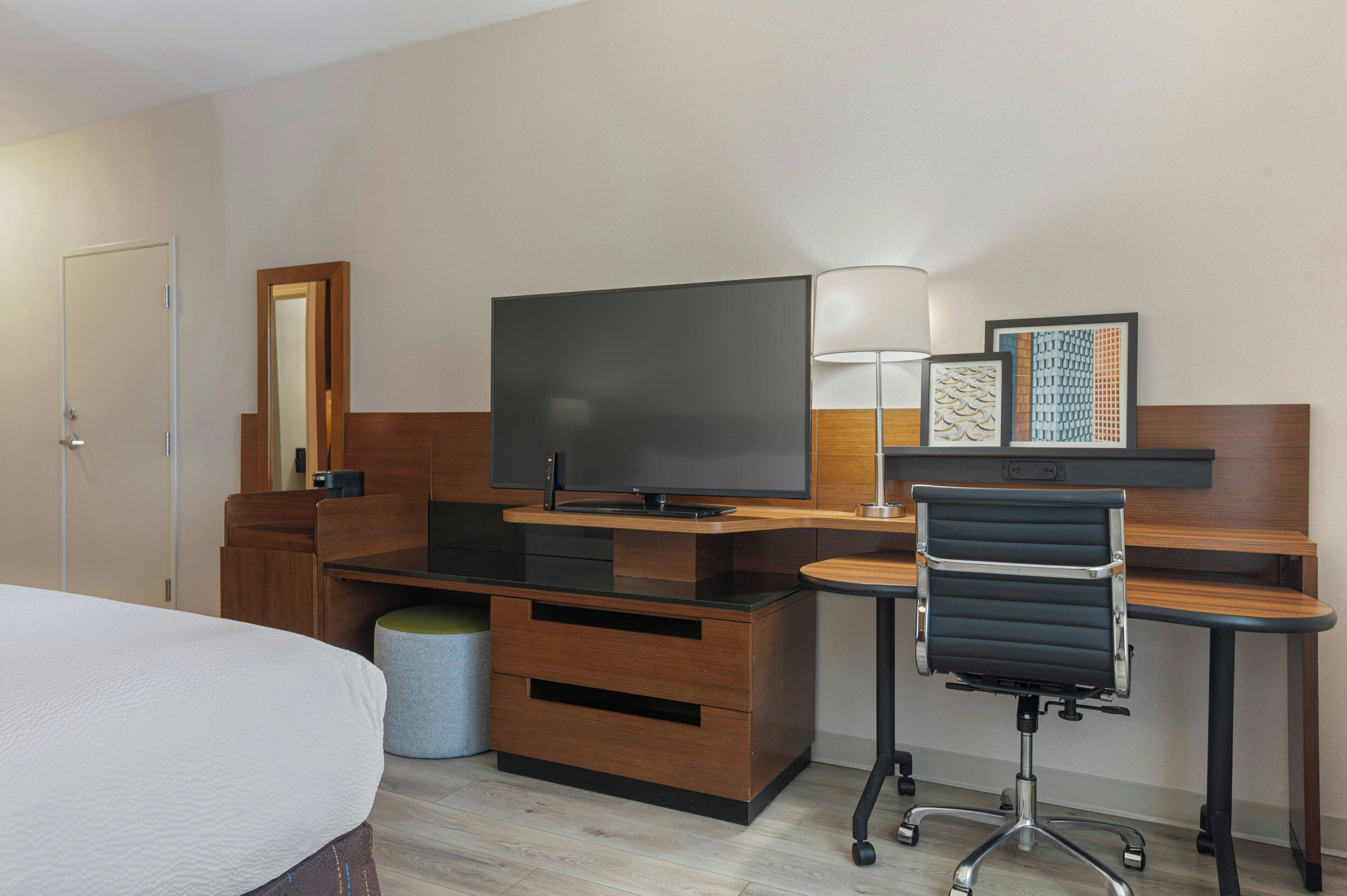 A hotel room with a bed, a desk with a computer, a TV, a chair, and a small round table.
