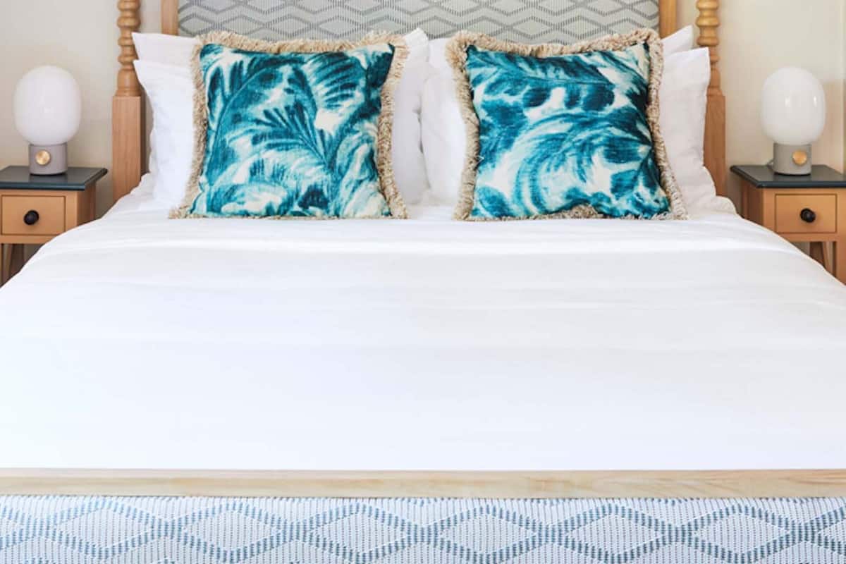 A bed with a wooden headboard, two matching pillows, and a macrame wall hanging.