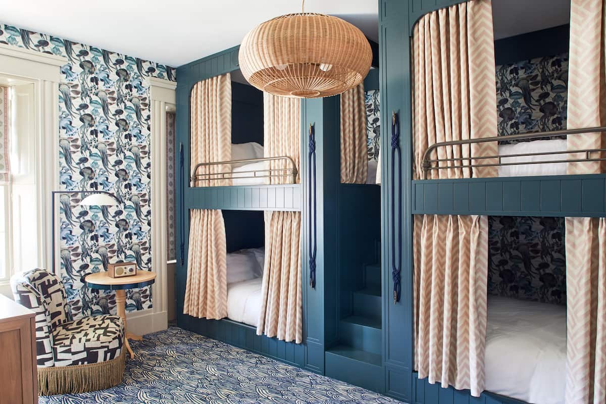 A room with bunk beds, a woven light fixture, a patterned chair, and a small table.
