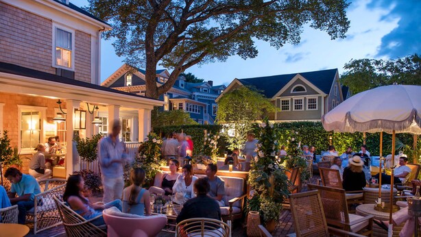An outdoor patio area with wicker furniture, brick flooring, and a variety of plants. - Faraway Nantucket (Nantucket)