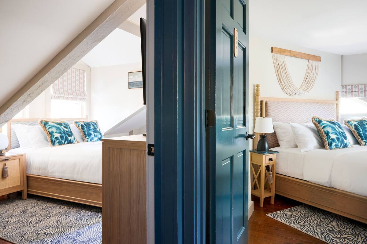 A bedroom with two beds, a wooden headboard, a nightstand, a lamp, and a patterned rug.
