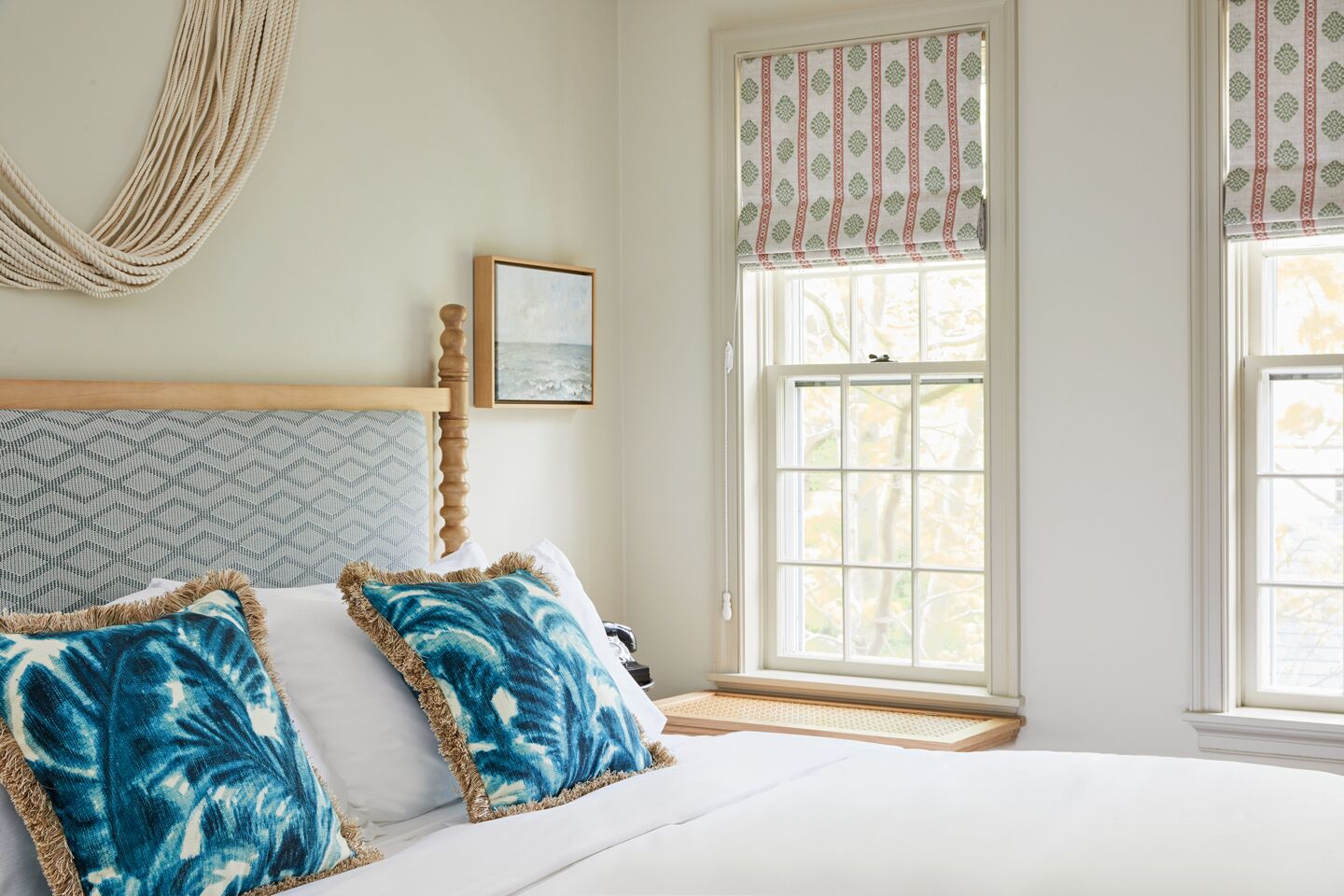 A bedroom with a bed, a window with a view, a hanging chair, and a framed picture on the wall.