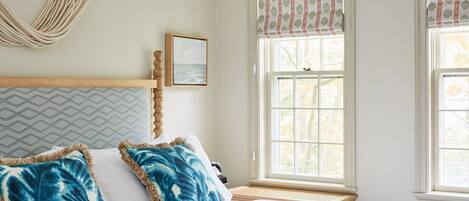 A bedroom with a bed, a window with a view, a hanging chair, and a framed picture on the wall.