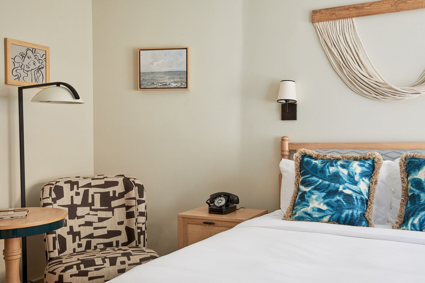 A hotel room with a bed, a chair, a bedside table with a lamp, a wall clock, and a framed picture.