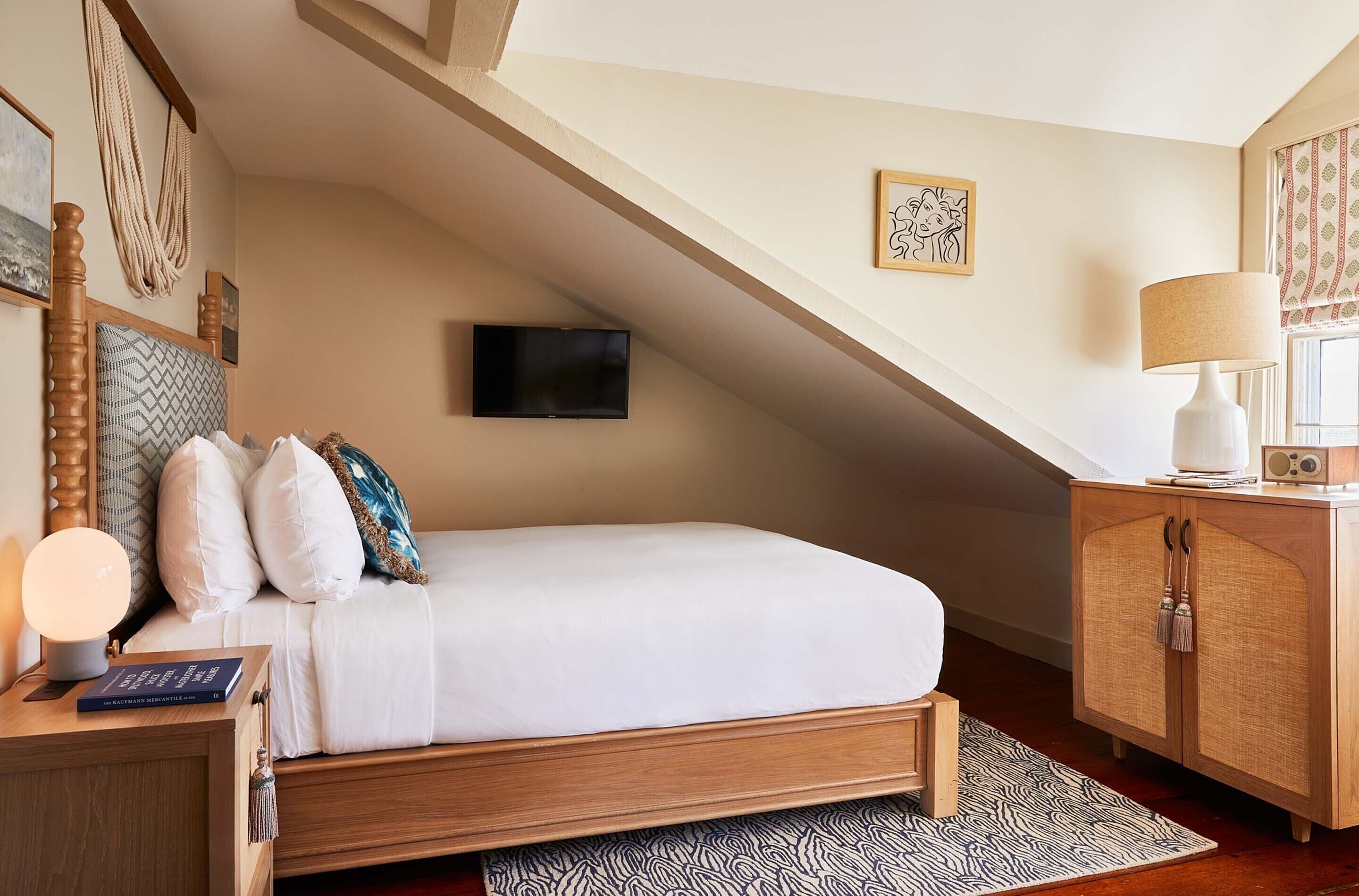 A bedroom with a wooden bed, a bedside table with a lamp, a TV mounted on the wall, and a cabinet.