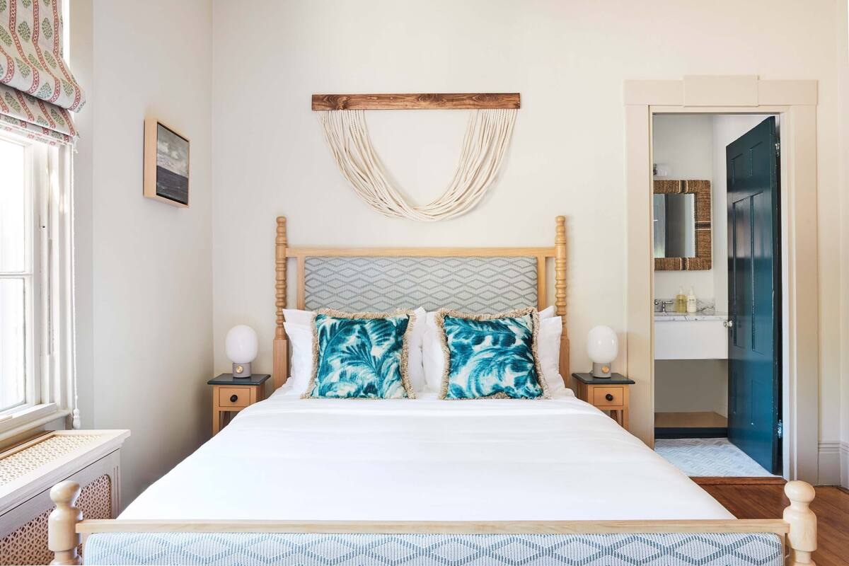 A neatly made bed with a wooden headboard, two matching pillows, and a bedside table with a lamp.