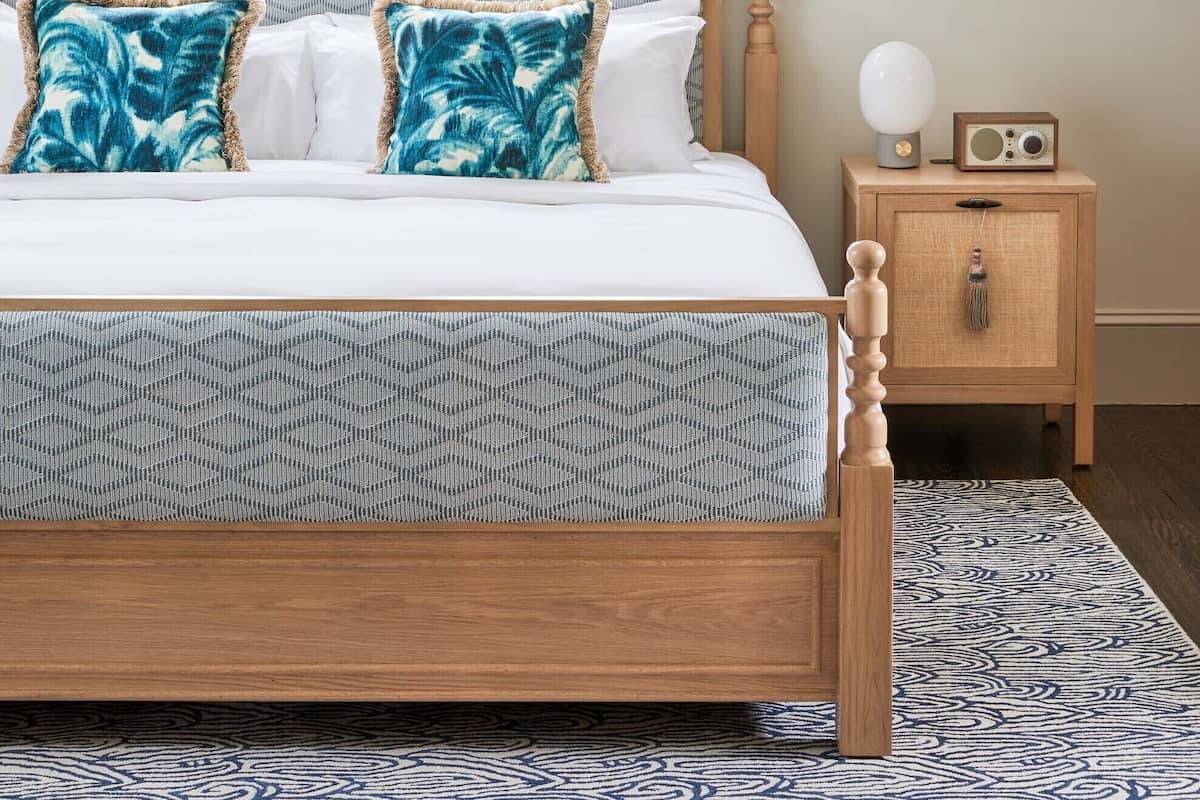 A bedroom with a wooden bed, patterned pillows, a nightstand with a radio, and a view of the ocean through windows.
