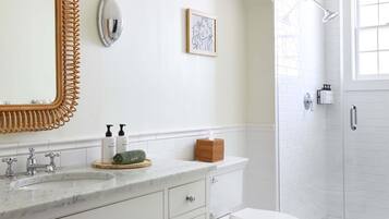 Un bany amb un lavabo blanc, un mirall gran, un vàter i una dutxa a celobert.