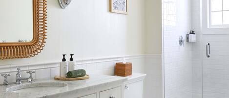 A bathroom with a white vanity, a large mirror, a toilet, and a walk-in shower.
