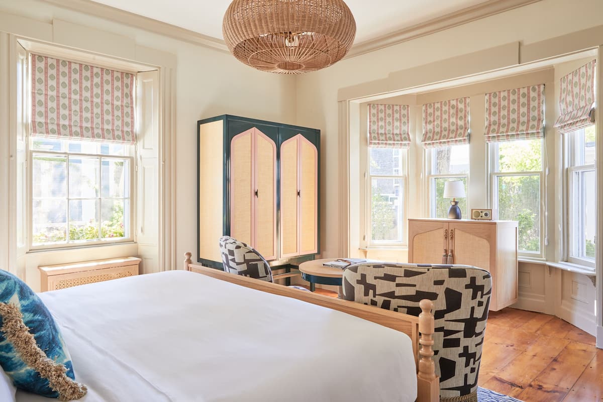 A bedroom with a large bed, a wooden wardrobe, a round table, and patterned chairs.