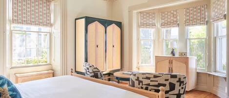 Een slaapkamer met een groot bed, een houten garderobe, een ronde tafel en gestreept stoelen.