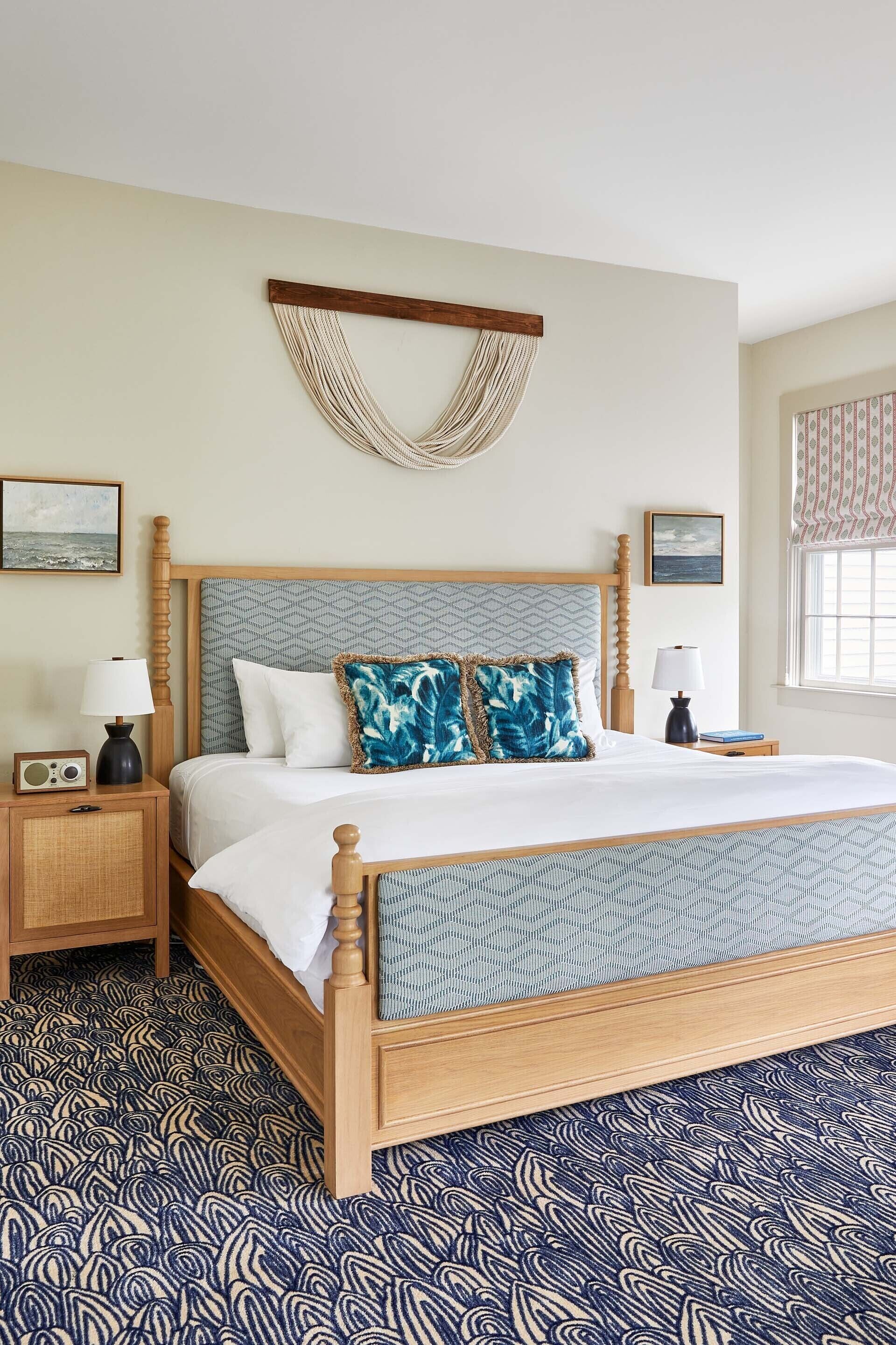 A neatly arranged bedroom with a wooden bed, two bedside tables, a wall-mounted macrame piece, and patterned carpet.