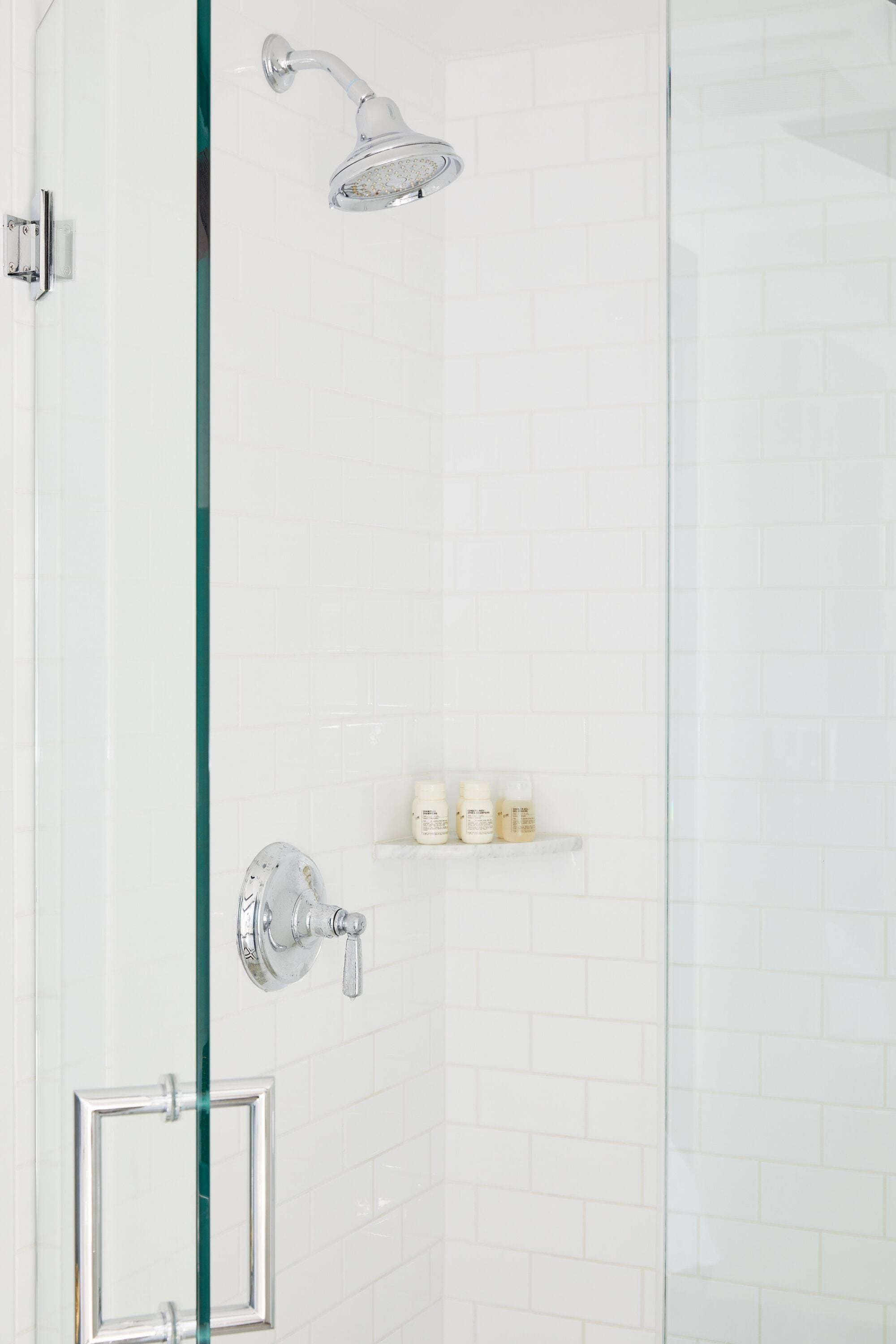 A glass-enclosed shower with chrome fixtures and a white tiled wall.