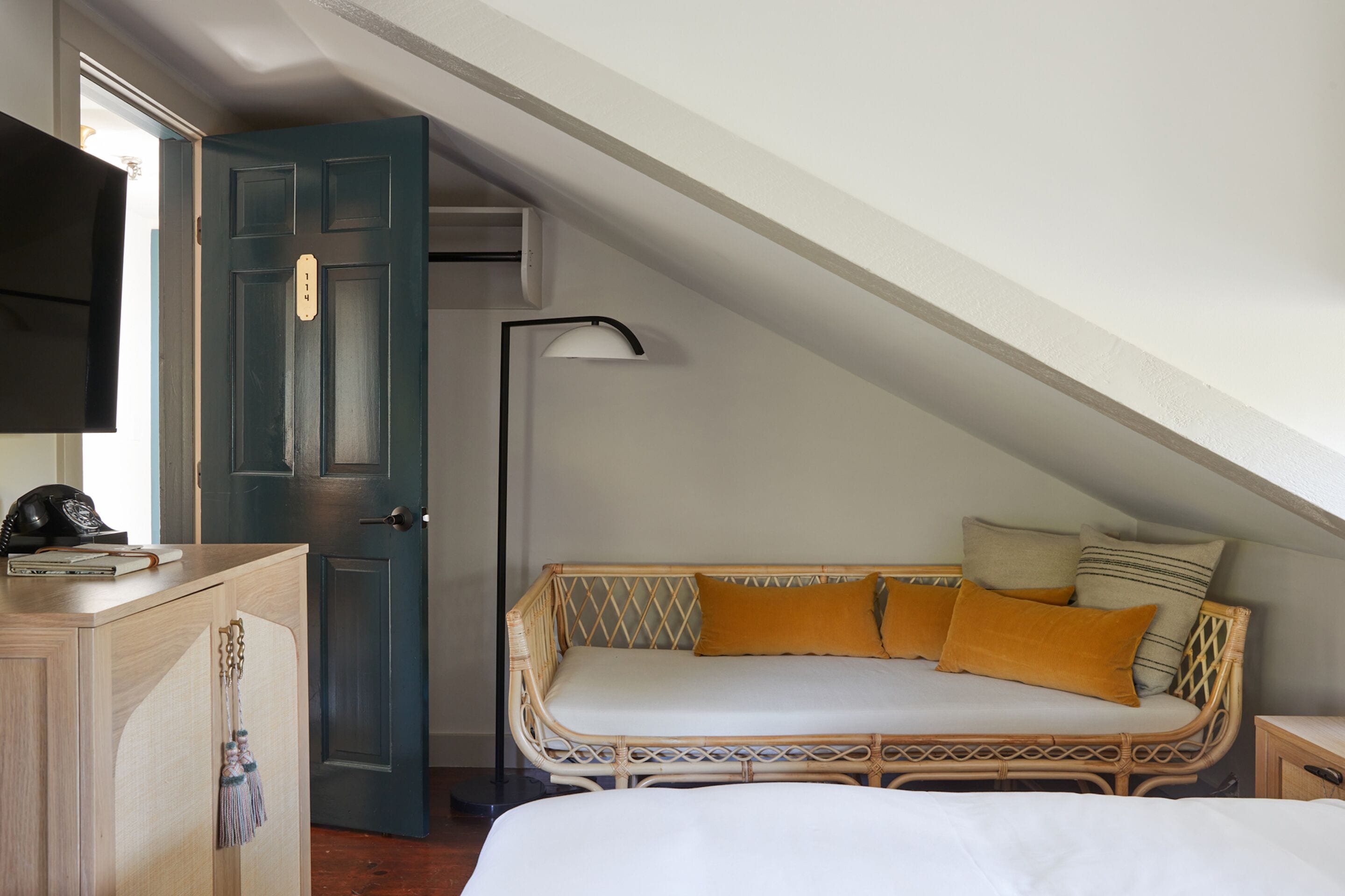 A bedroom with a bed, a sofa bed with cushions, a wardrobe, and a desk with a lamp.
