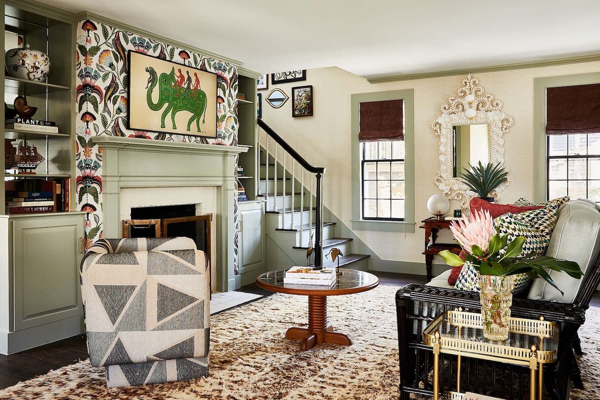 A living room with a patterned wall, a fireplace, a staircase, and a large mirror.