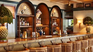 A bar area with wooden bar counters, wicker chairs, and shelves with bottles. - Faraway Nantucket (Nantucket)