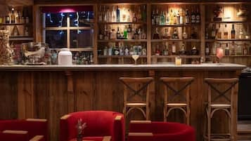 Uma área de bar com estantes de madeira repletas de garrafas, balcão e cadeiras estofadas em vermelho.