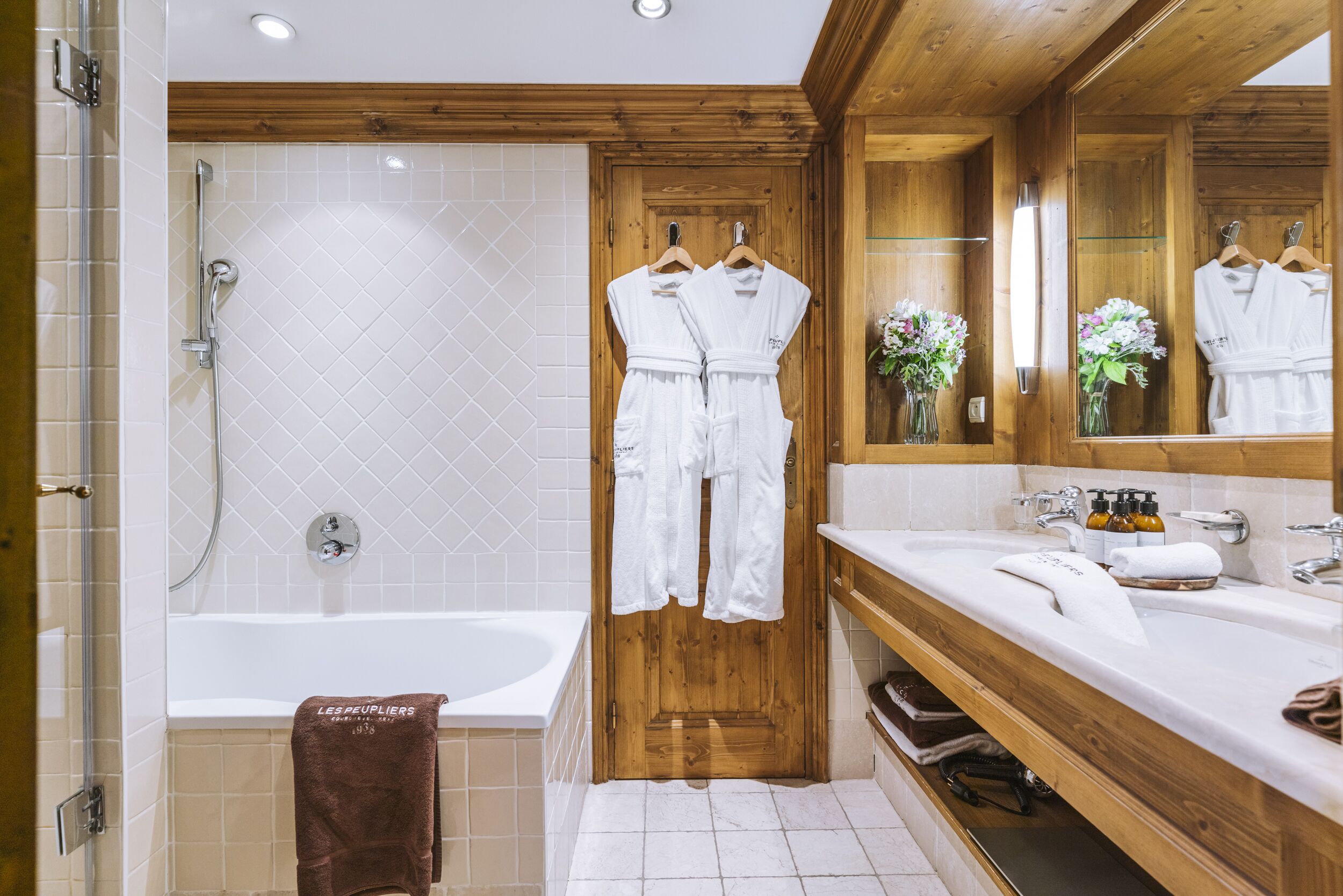 A modern bathroom with a wooden door, a bathtub, a shower, and a vanity with a mirror.