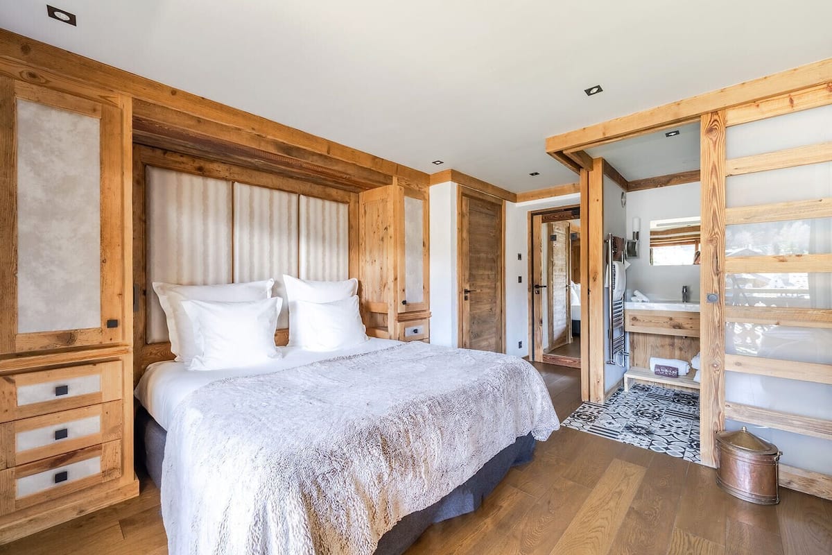 A bedroom with a wooden headboard, a large bed with white linens, a wooden dresser, and a mirror.