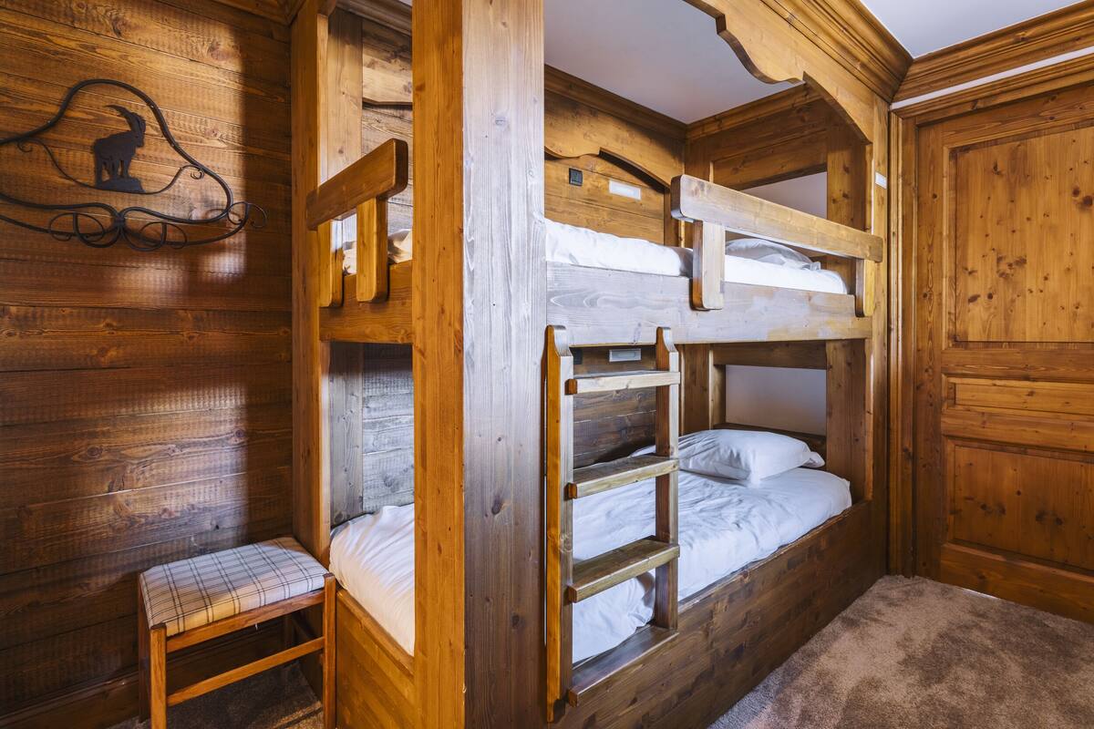 A rustic wooden cabin room with bunk beds, a small bench, and a decorative wall piece.