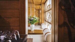 Een houten interieur met een witte vaas met bloemen op een houten bankje, een houten leuning en een houten vloer.