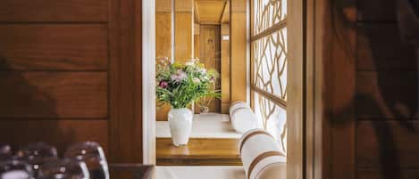 Un intérieur en bois, avec un vase blanc rempli de fleurs posé sur un banc en bois, une balustrade en bois et un plancher en bois.