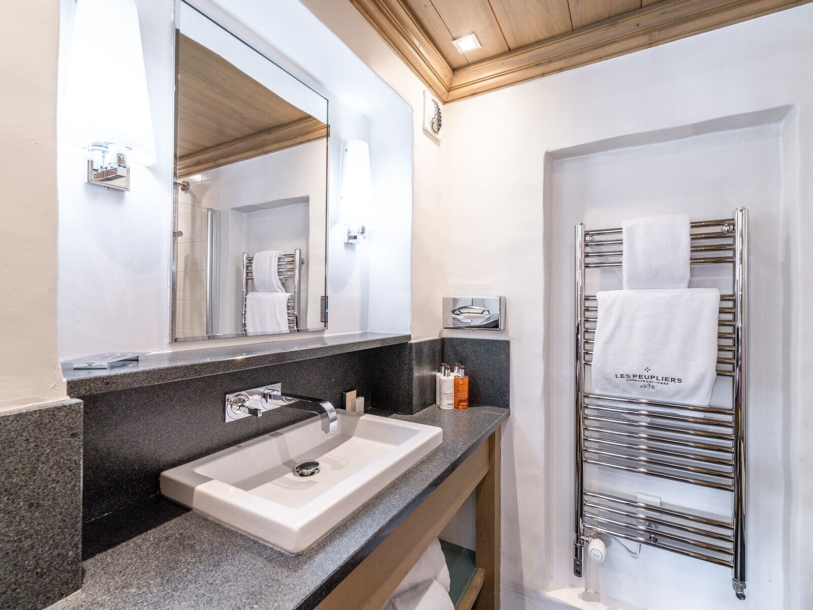 Un baño moderno con un espejo grande, un lavamanos, un perchero para toallas y una zona de ducha.