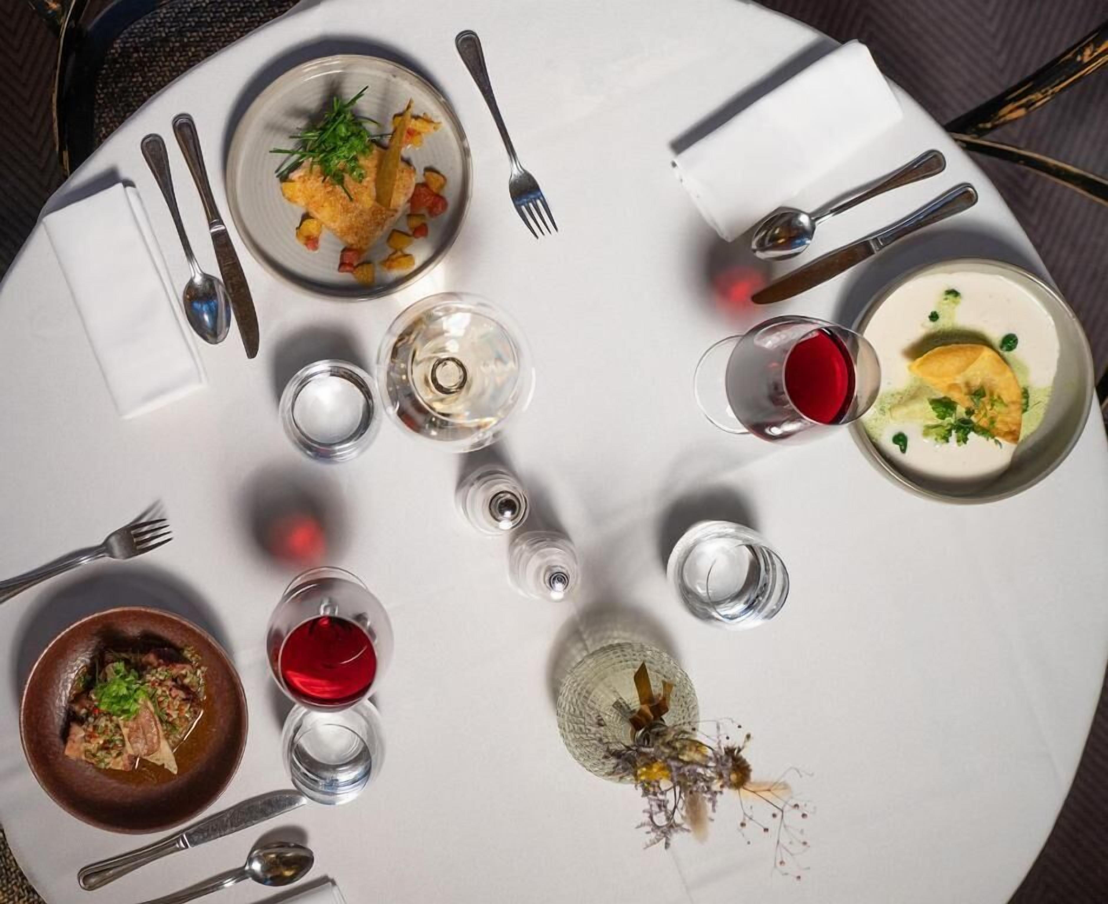 A round dining table with plates of food, glasses of red wine, and cutlery.