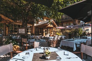 Un espace de restauration en plein air, avec des tables et des chaises, entouré d’arbres et bordé d’un bâtiment à la façade en bois.