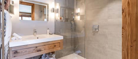 A modern bathroom with a wooden vanity, a glass shower enclosure, and a large mirror.