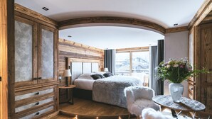 Een gezellig slaapkamer met een houten plafond, een bed met een zachte deken, een klein rond tafeltje met een bloevas, en een comfortabele fauteuil.