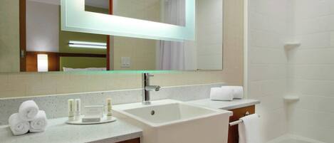 A bathroom with a large mirror, a sink, a bathtub, and a vanity with toiletries.