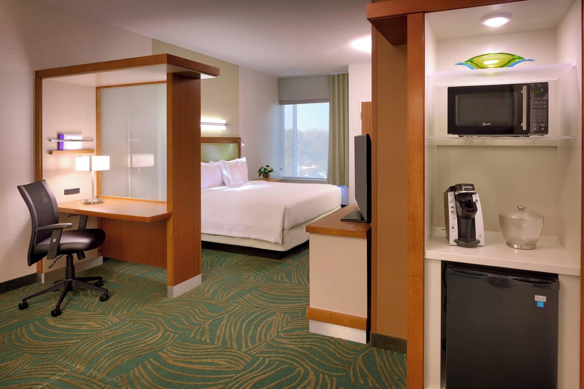 Une chambre d’hôtel équipée d’un lit, d’un bureau, d’une chaise, d’un four à micro-ondes, d’un réfrigérateur et d’une fenêtre donnant sur un paysage agréable.