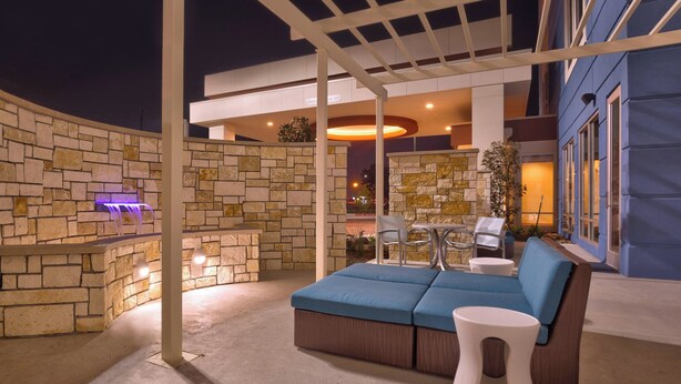 An outdoor patio area with a stone wall, a blue cushioned seating area, and a small table with chairs. - Springhill Suites Houston I-45 North (Houston)