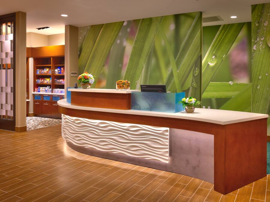 A reception desk with a modern design, a water feature, and a backdrop of green leaves.