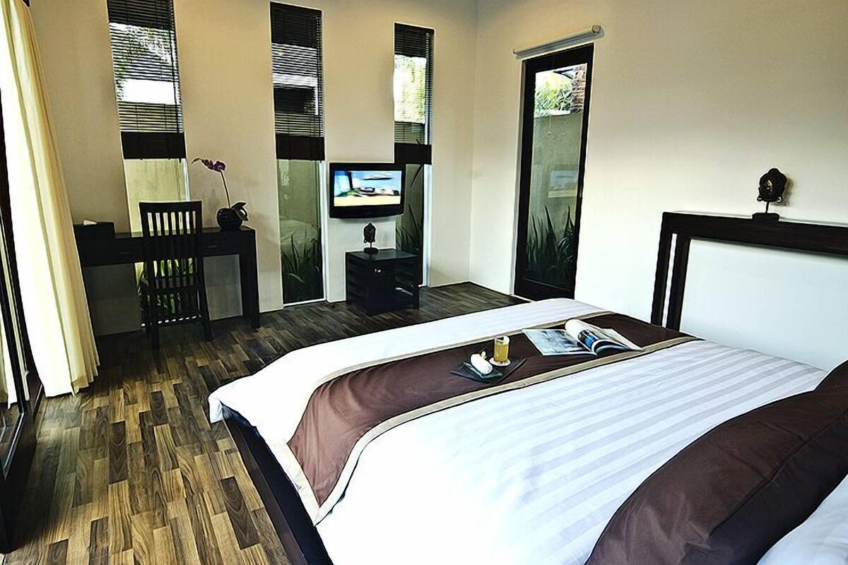 A modern hotel room with a large bed, a desk with a chair, a television, and a sliding glass door.