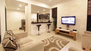 Una sala de estar moderna con un sofá, un televisor y una cocina al fondo.