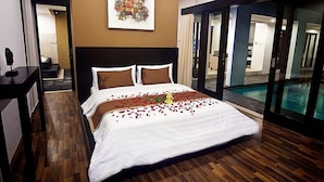 Habitación de hotel con una cama grande, piso de madera, un cuadro en la pared y vista a una piscina.
