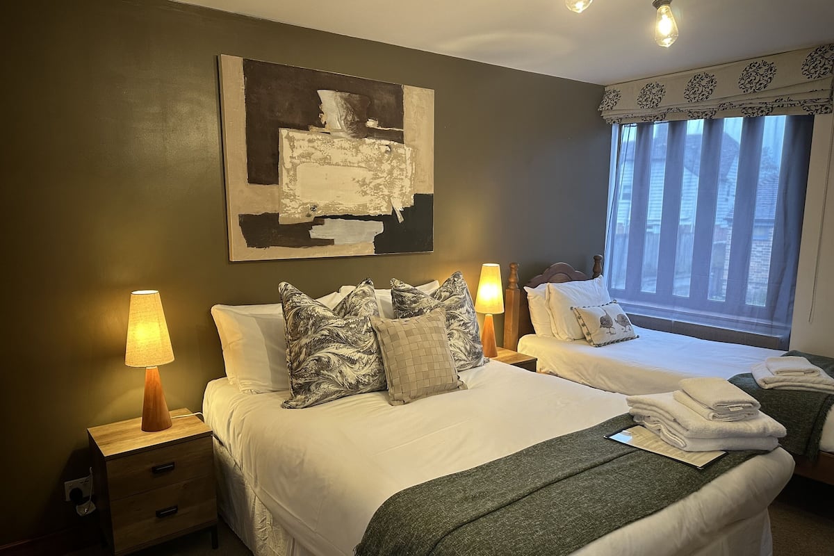 A hotel room with two beds, a large abstract painting on the wall, and a window with curtains.