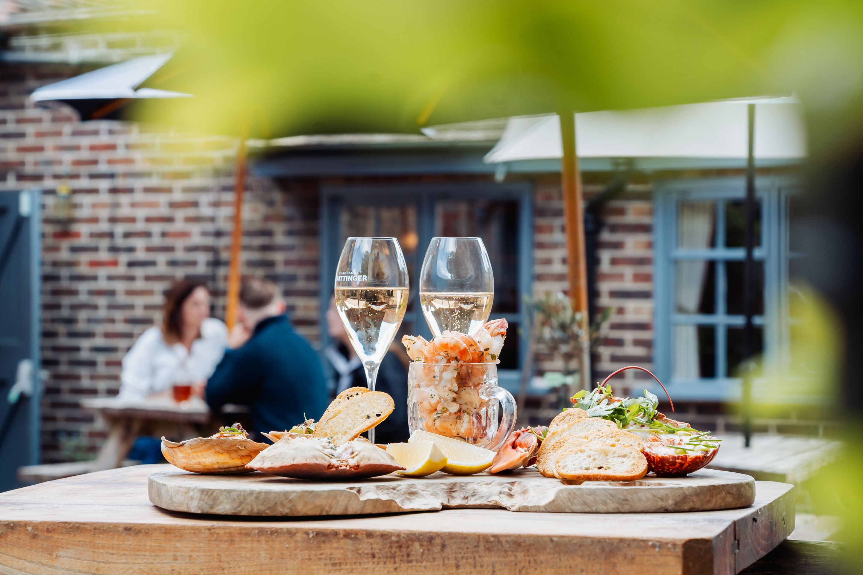 Una mesa de comedor con platos de mariscos, una jarra de camarones y dos copas de vino blanco.