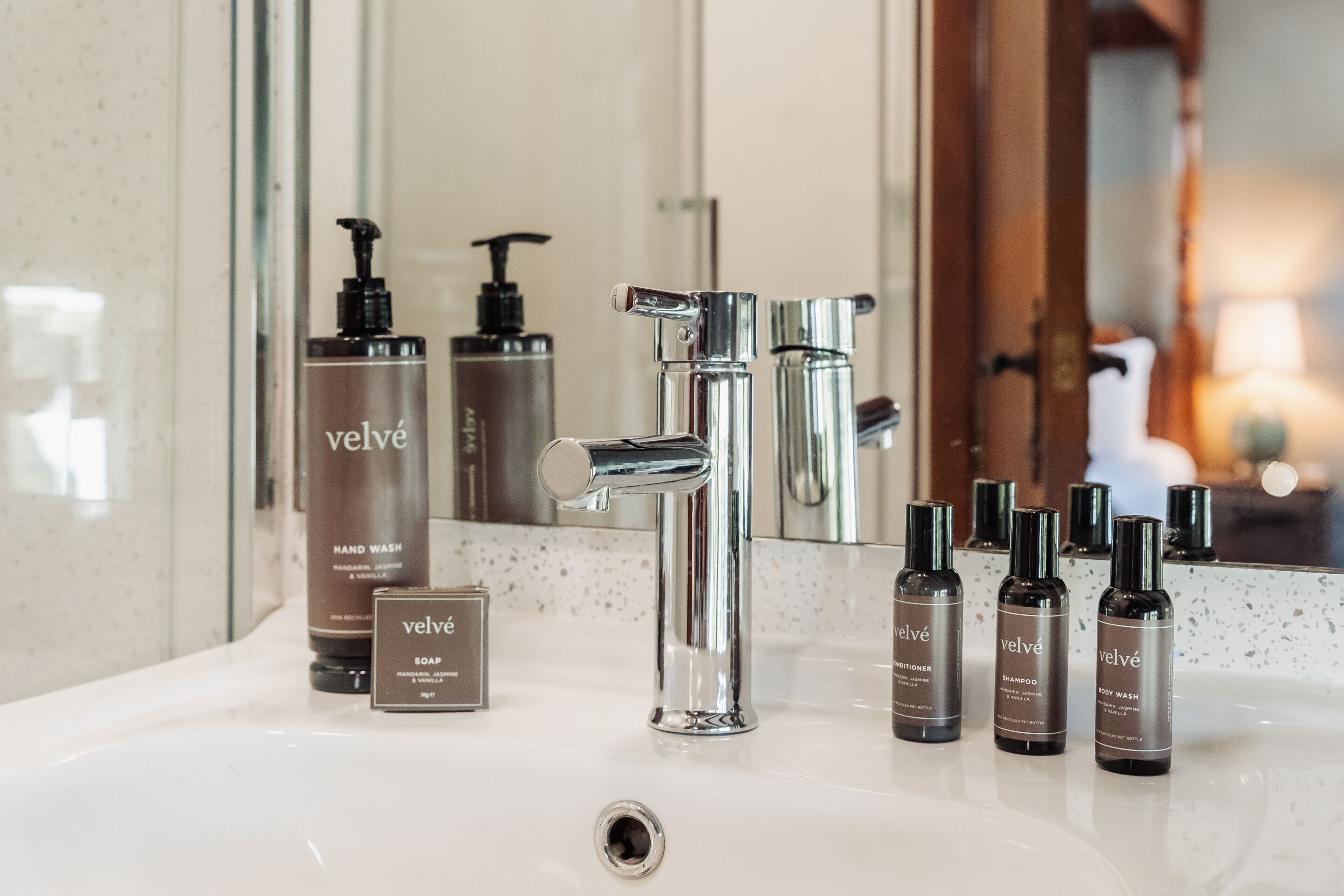 A bathroom with a chrome faucet, a mirror, and various toiletries including hand wash, soap, shampoo, and body wash.