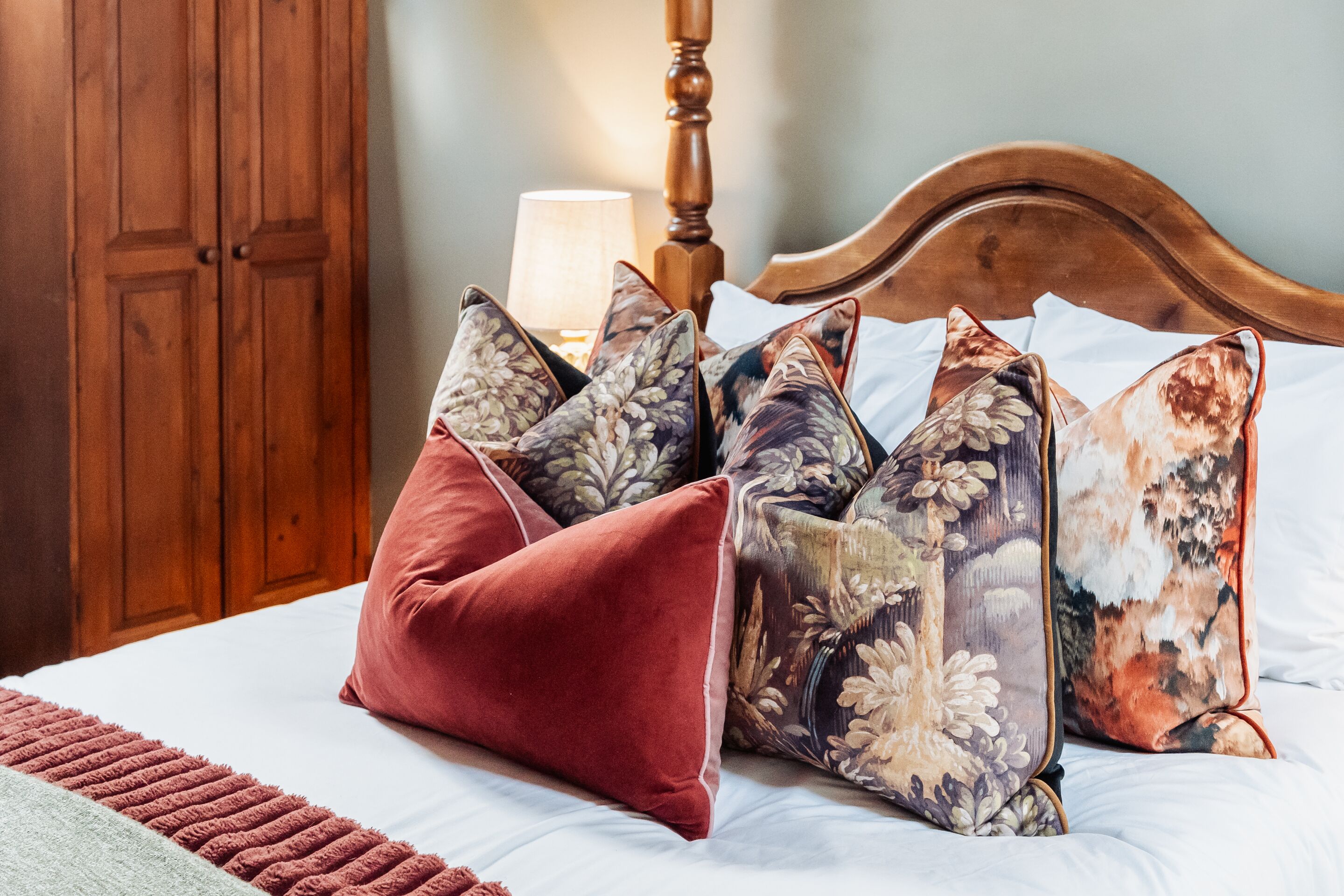 A bed with floral-patterned pillows, a wooden headboard, and a wooden wardrobe in the background.