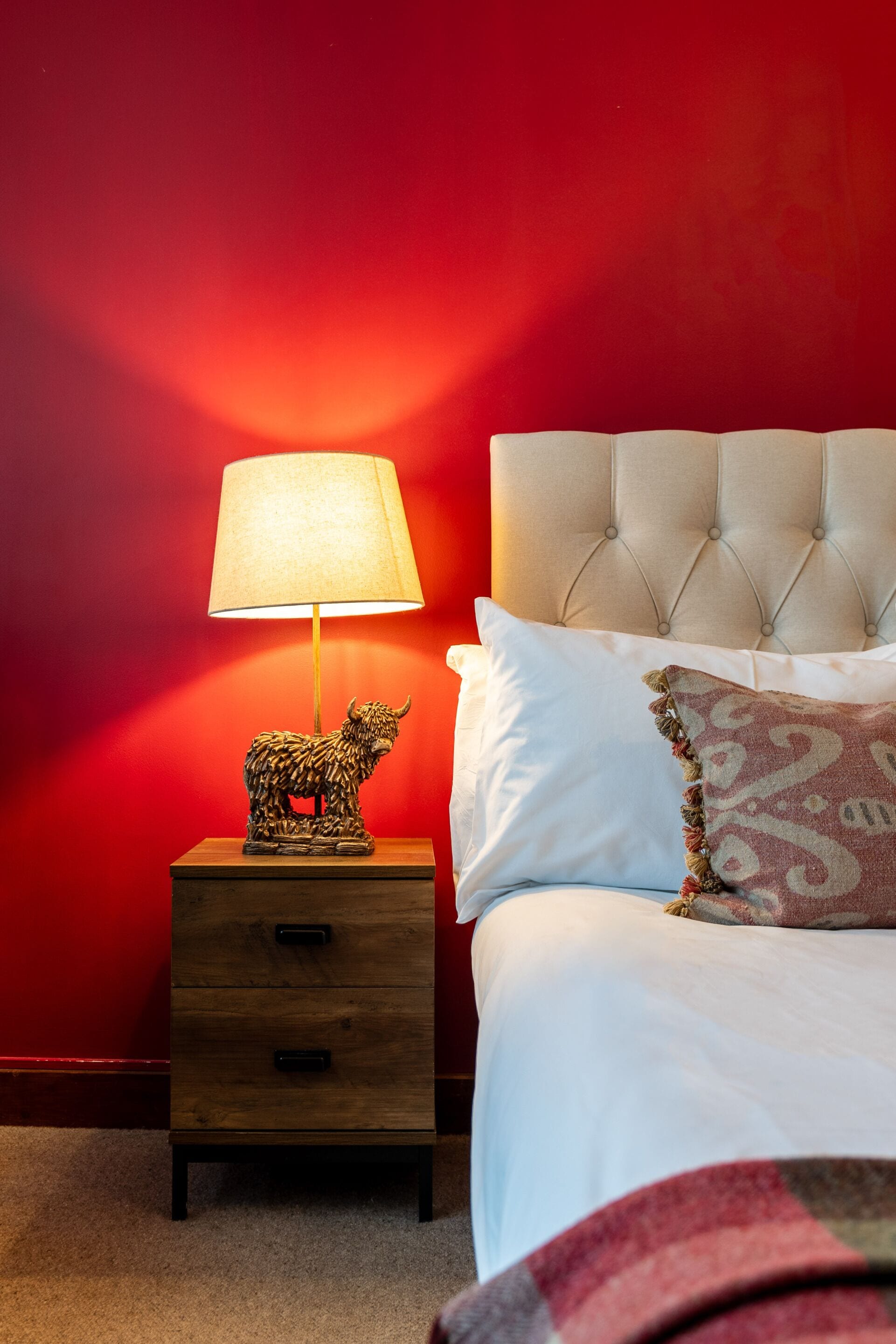 A bedroom with a red wall, a bedside table with a lamp, and a bed with white bedding.