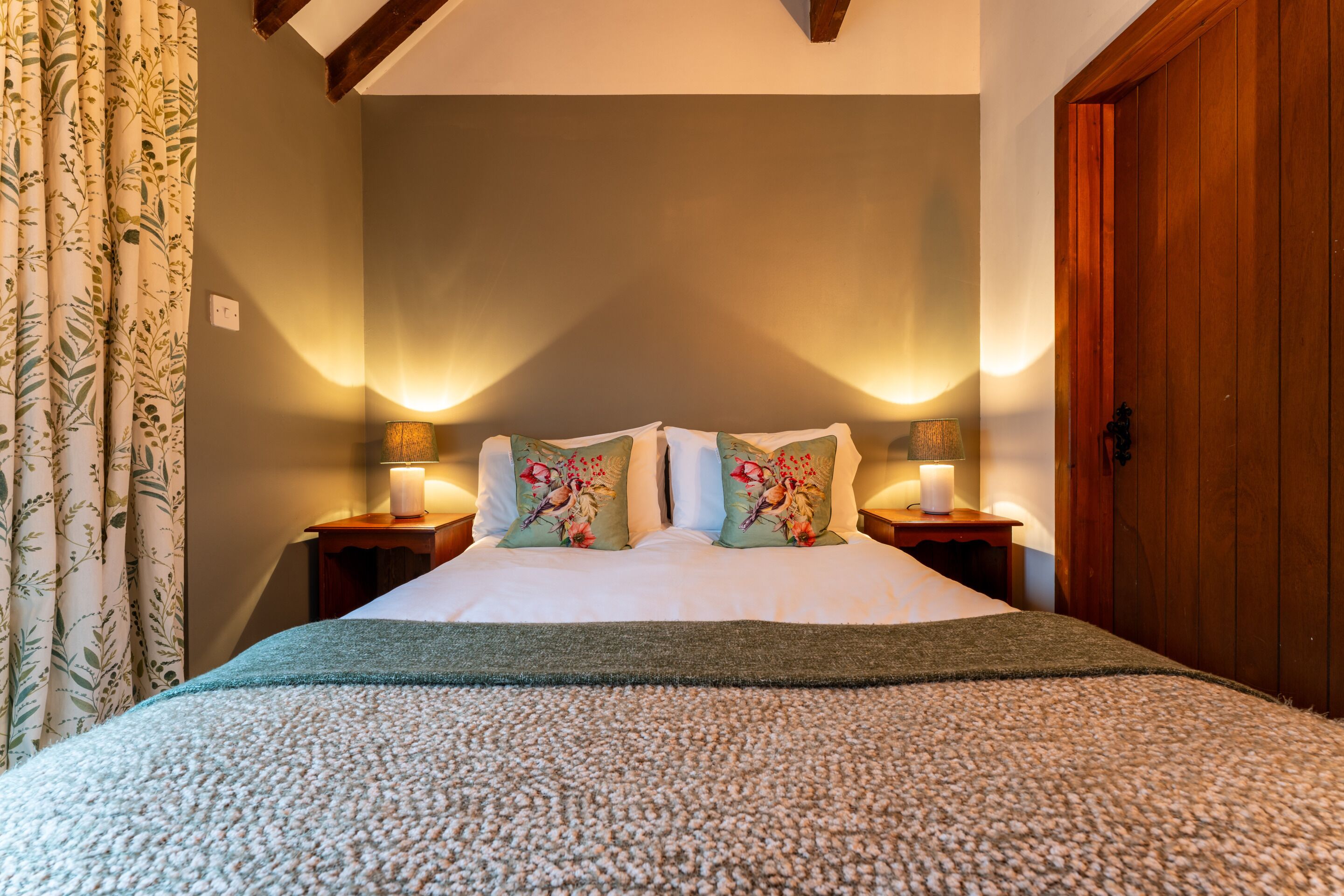 A neatly made bed with floral pillows, a green throw blanket, and two bedside lamps.