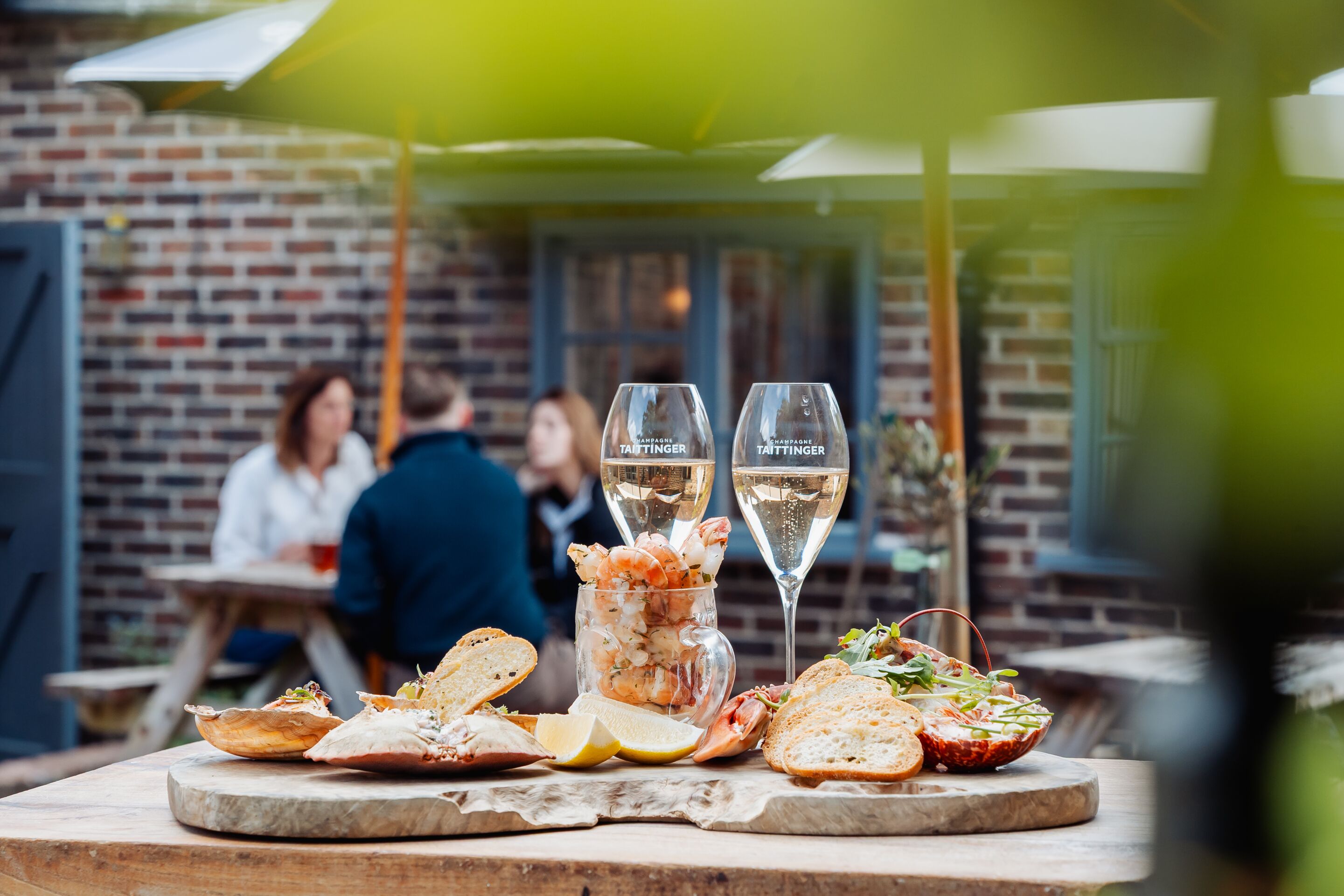 A dining table with seafood dishes, two glasses of champagne, and a brick wall background.