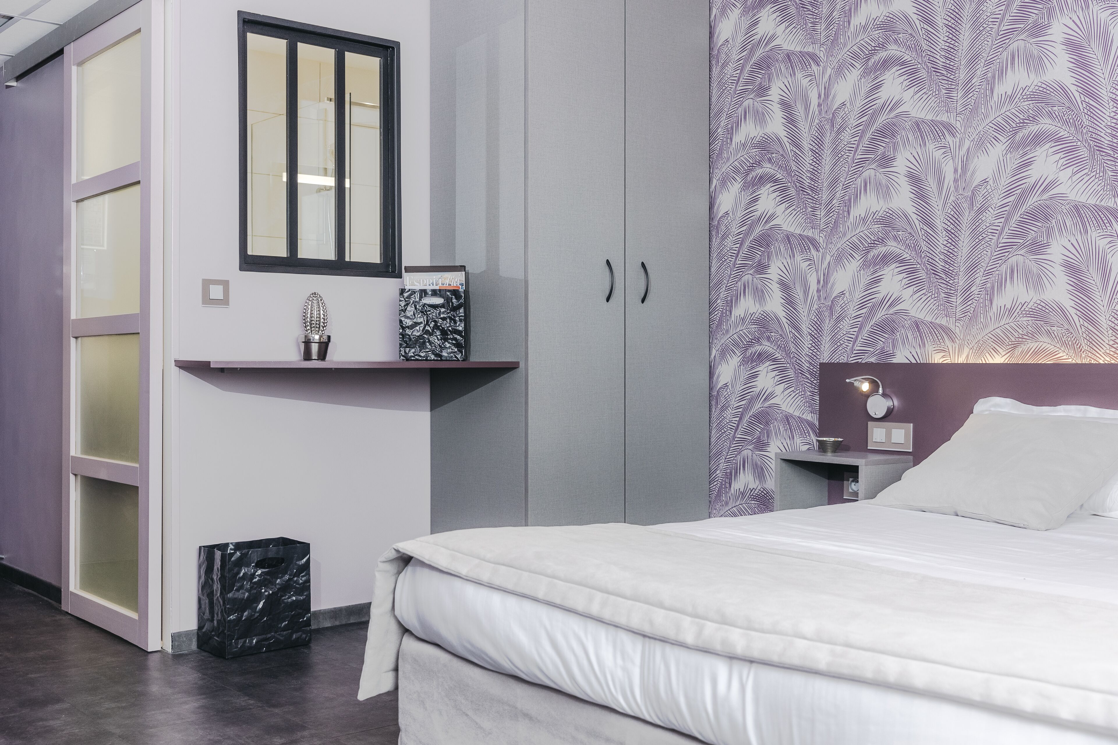 Ein Schlafzimmer mit Bett, Kleiderschrank, Nachttisch, Spiegel und einer Wand mit Blättermotiv.