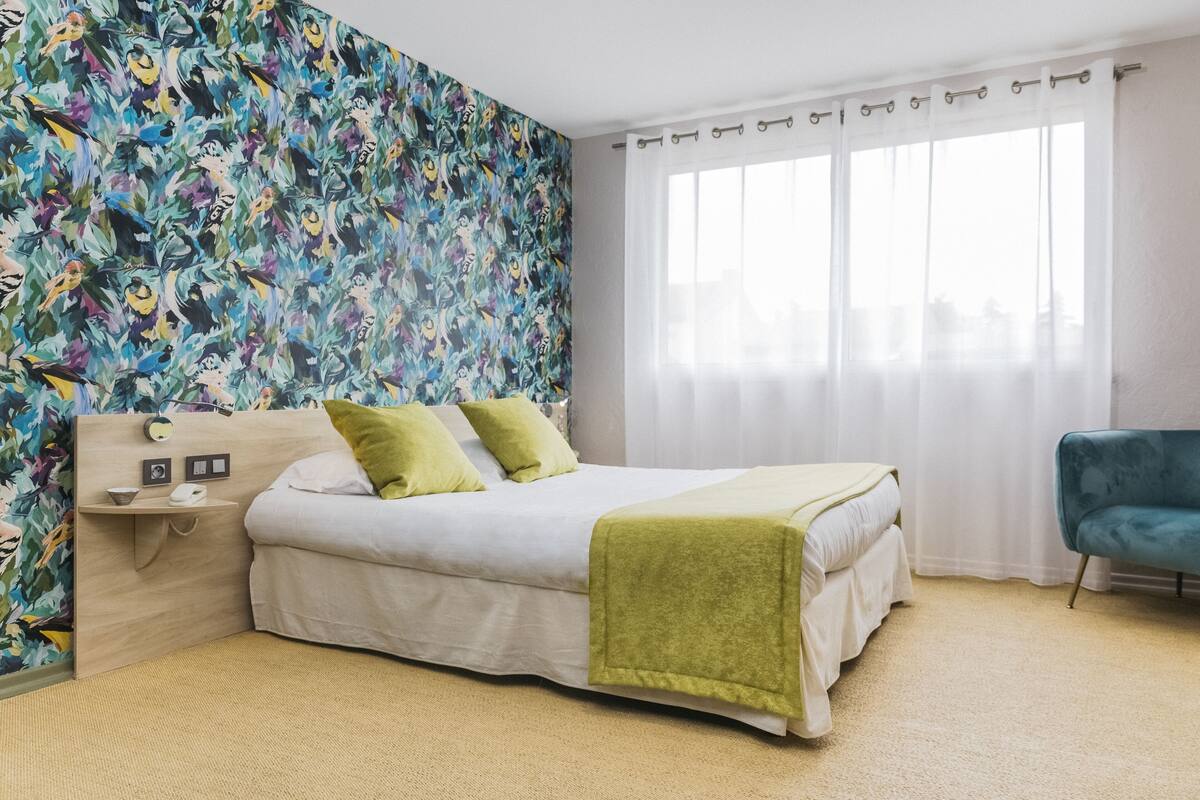 A bedroom with a bed, a nightstand, a chair, and a window with curtains.