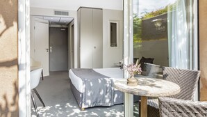 Une chambre moderne avec un lit, une petite table sur laquelle est posé un vase, et un fauteuil en osier.